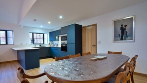 A modern kitchen with blue cabinets, a wooden dining table with chairs, and a painting on the wall. - Courtyard View at Longford (Longford)