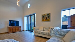 A spacious living room with a large sofa, a television on a wooden cabinet, and a painting on the wall. - Courtyard View at Longford (Longford)