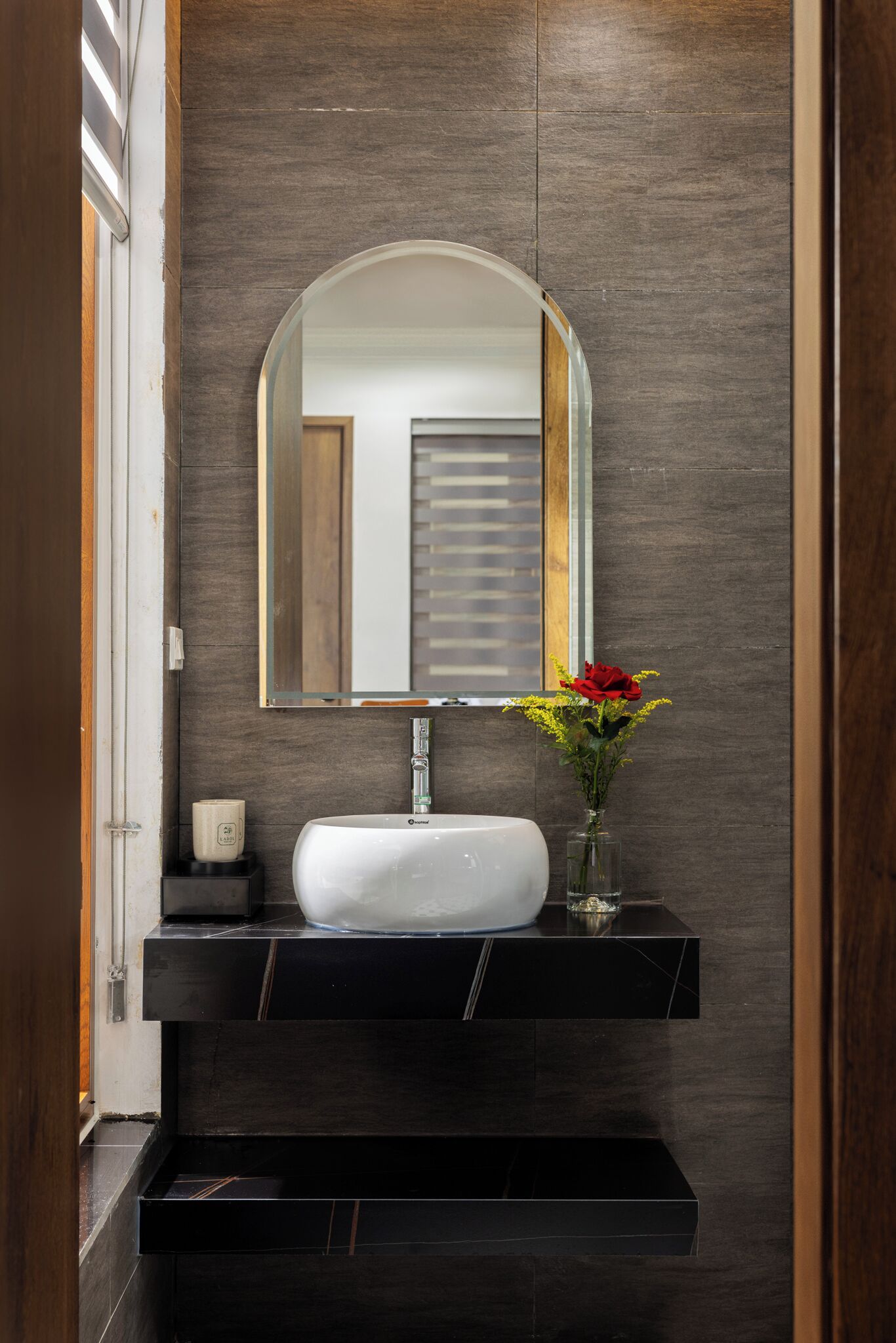A bathroom with a white sink, a mirror, and a vase with flowers.