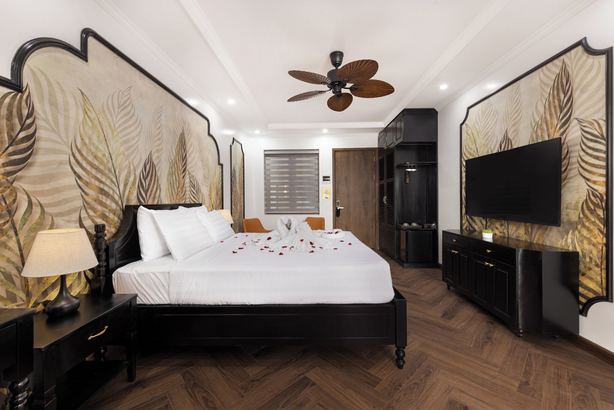 Un dormitorio con cama, ventilador de techo, televisor y suelo de madera.