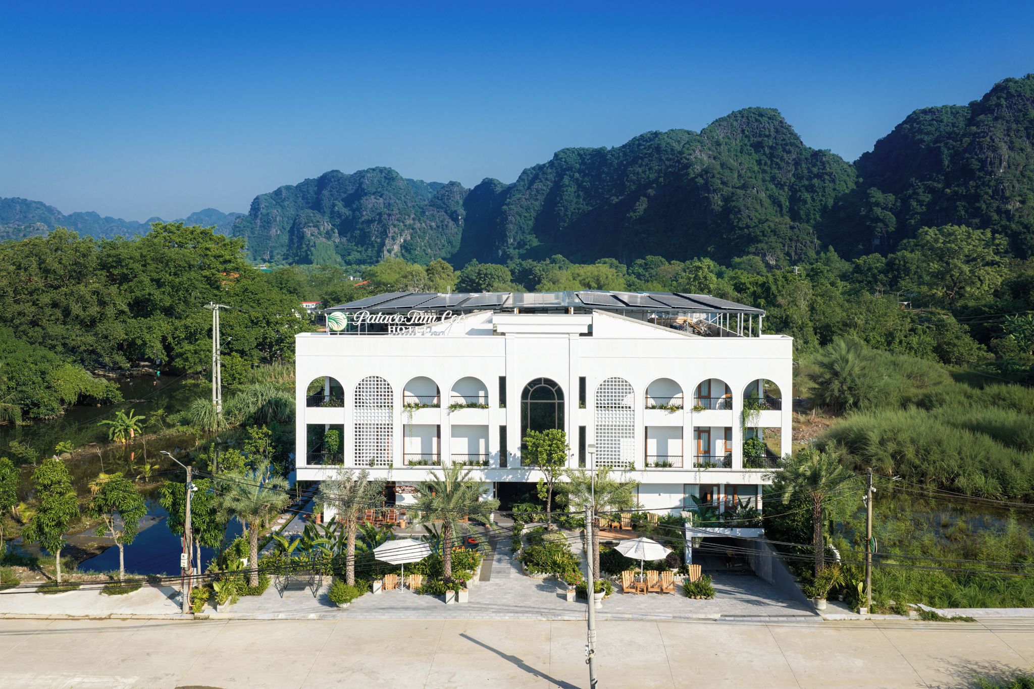 Un hotel moderno con tejado plano, varios balcones y vistas a exuberante vegetación y montañas.