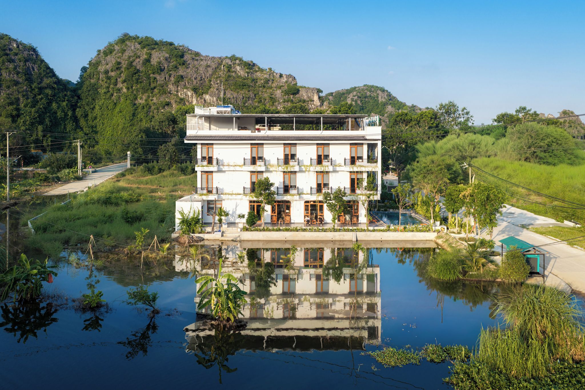 Hotel com vários andares, piscina em frente, cercado por vegetação e colinas.
