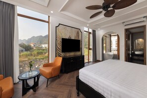 A hotel room with a large bed, a television mounted on the wall, a seating area with a table, and a view of the outdoors. - Pataco Tam Coc Hotel (Nam Hoa Lu)