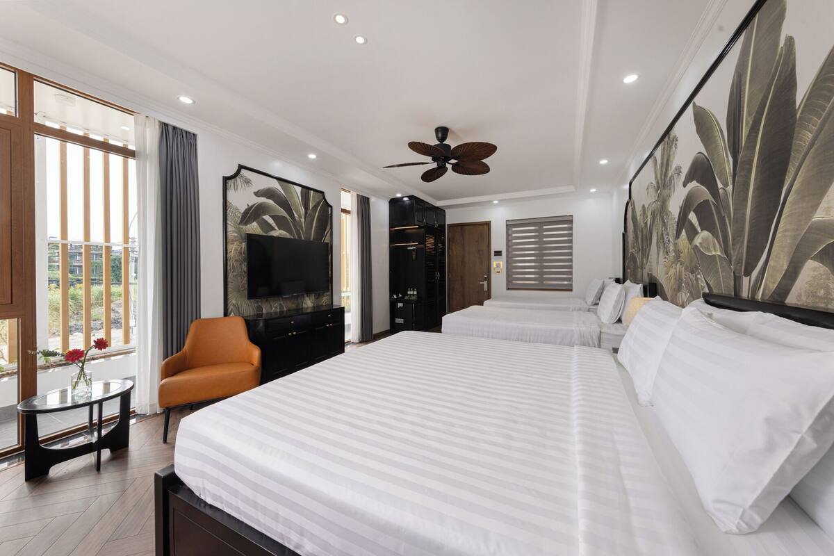 A hotel room with a large bed, a television, a seating area with a chair, and a large window with curtains.