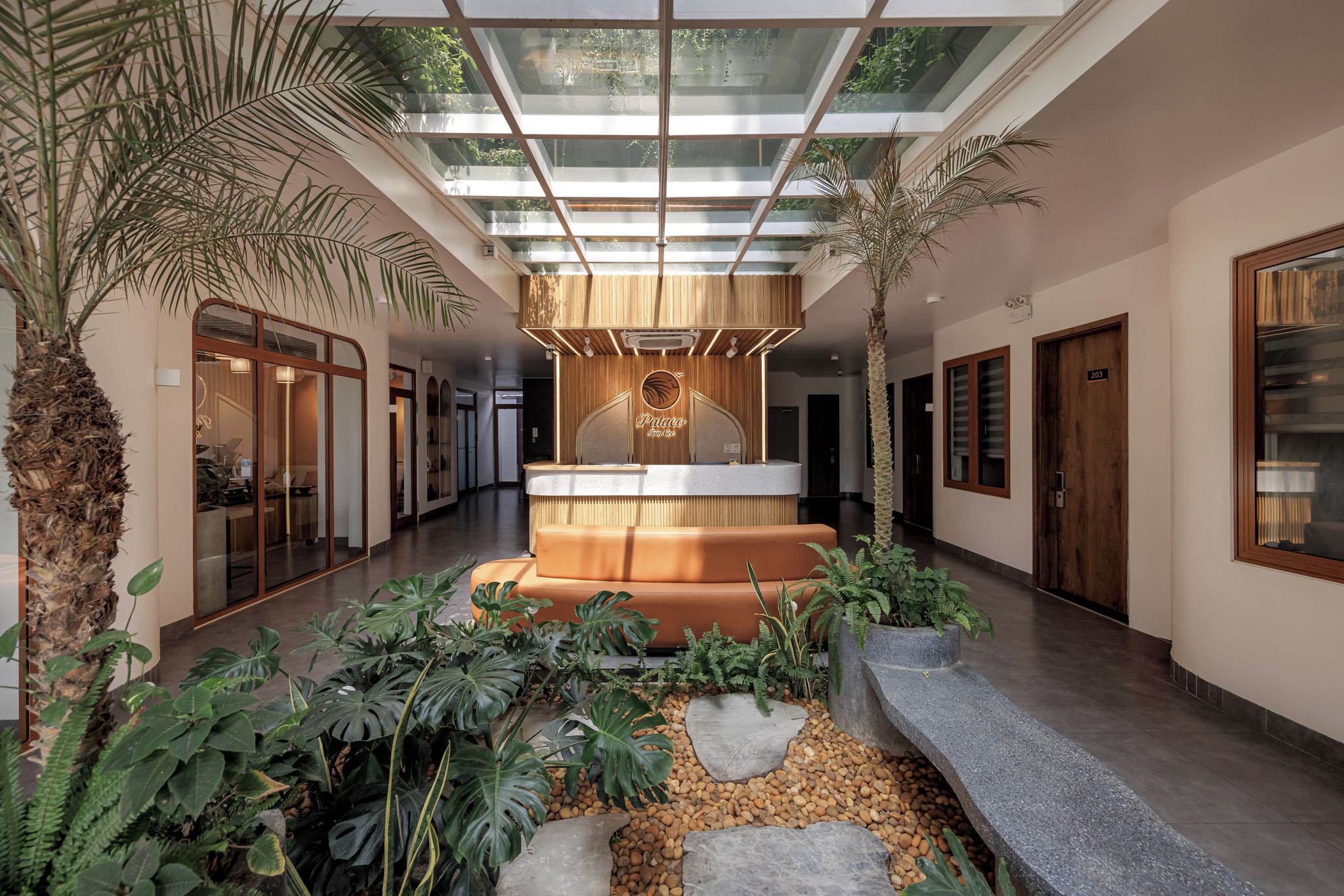 Un hall d’hôtel moderne doté d’un espace salon central, d’un plafond en verre et de plantes tropicales.