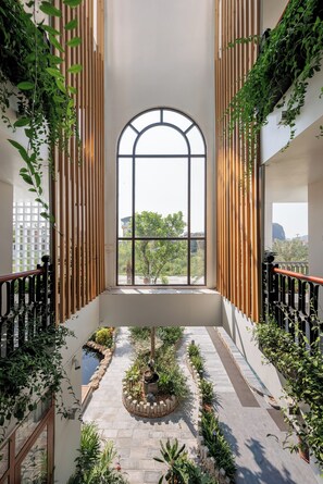A spacious atrium with a central garden, wooden slats on the walls, and a large arched window providing a view of the outdoors. - Pataco Tam Coc Hotel (Nam Hoa Lu)