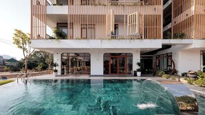 A modern building with a swimming pool, wooden balconies, and potted plants. - Pataco Tam Coc Hotel (Nam Hoa Lu)