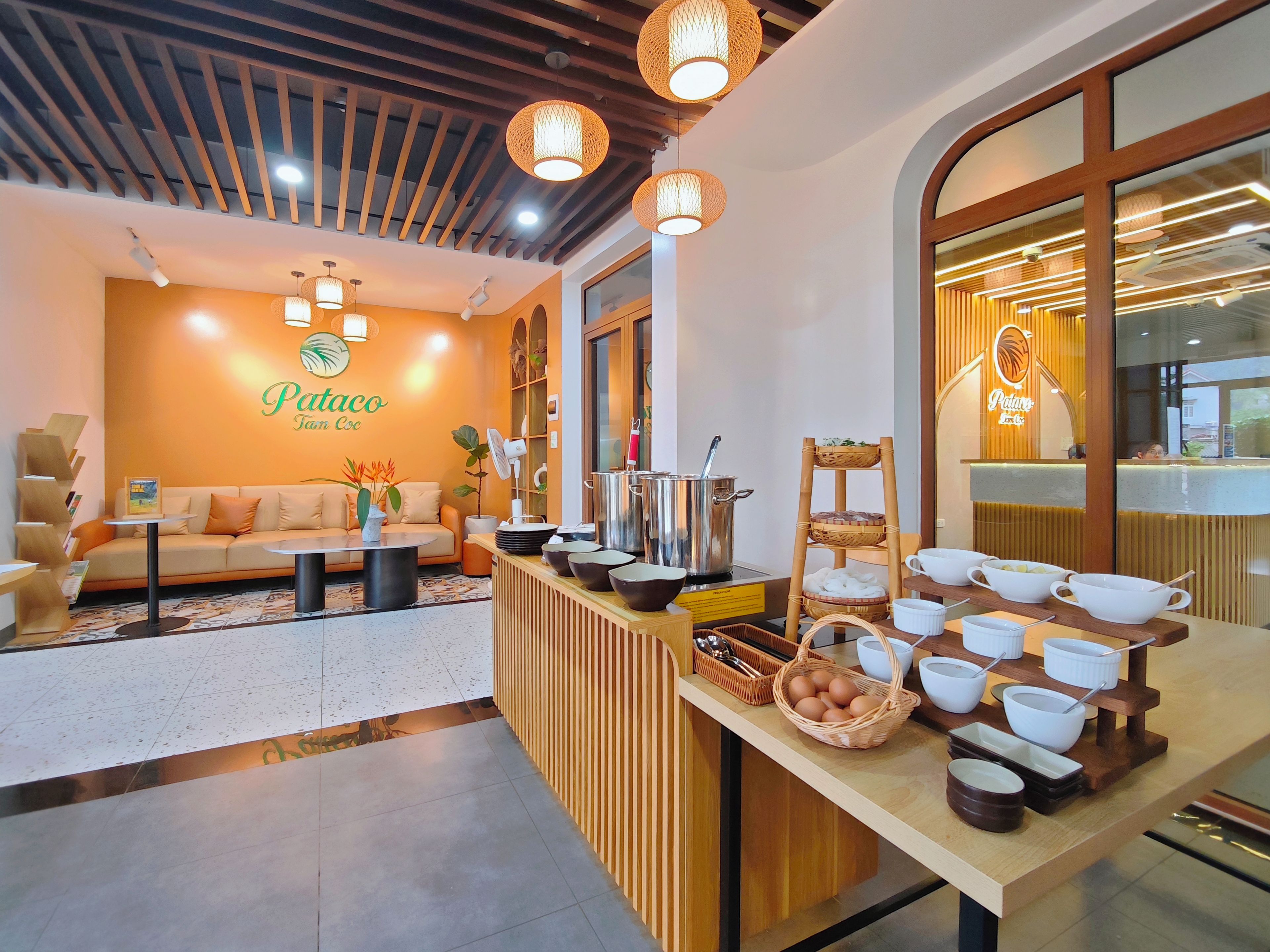 A restaurant with a modern interior, featuring a sofa, dining tables, and a counter with bowls and utensils.