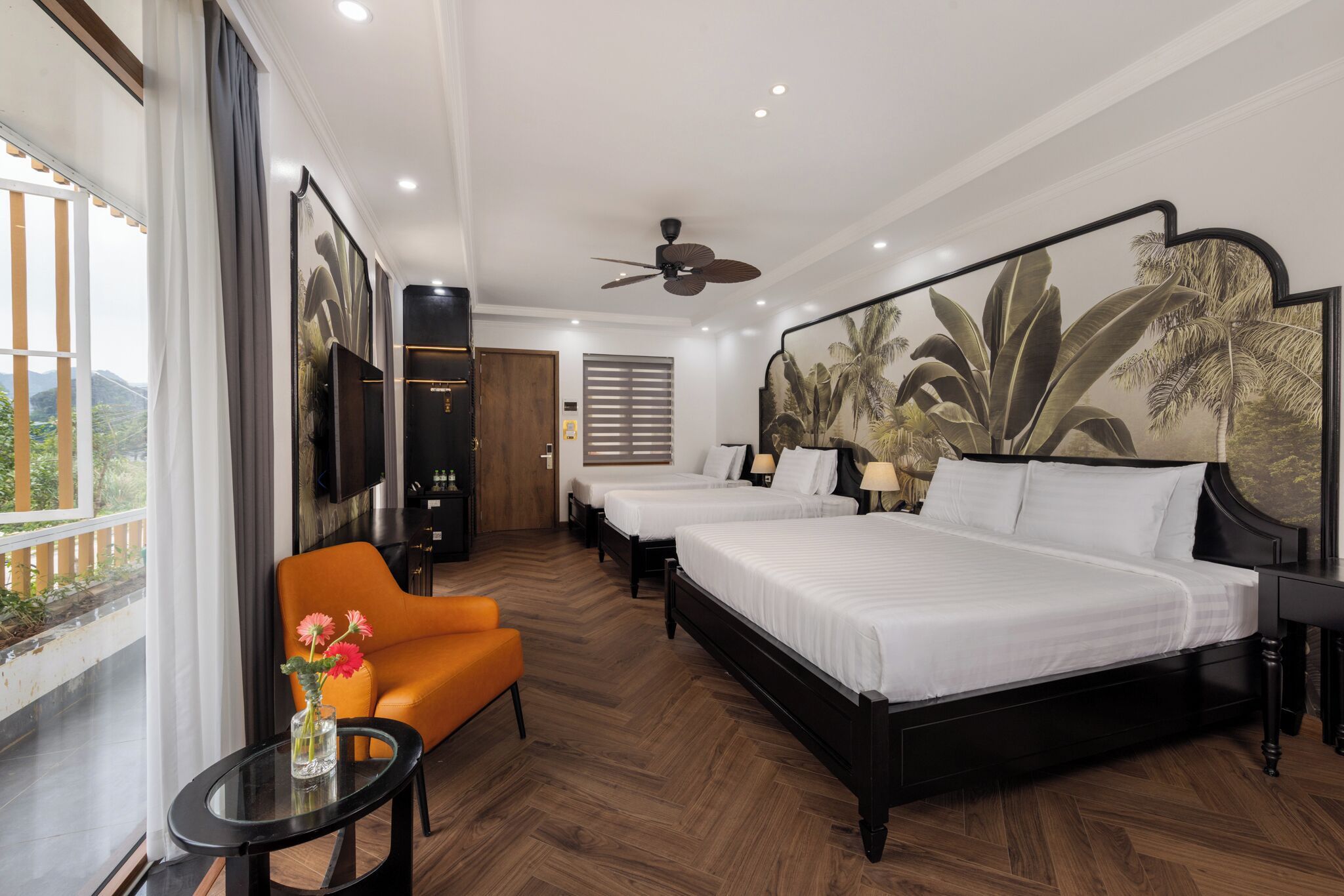 Een hotelkamer met twee bedden, een bank, een kleine tafel met een vaas, en een groot raam met uitzicht op groen.