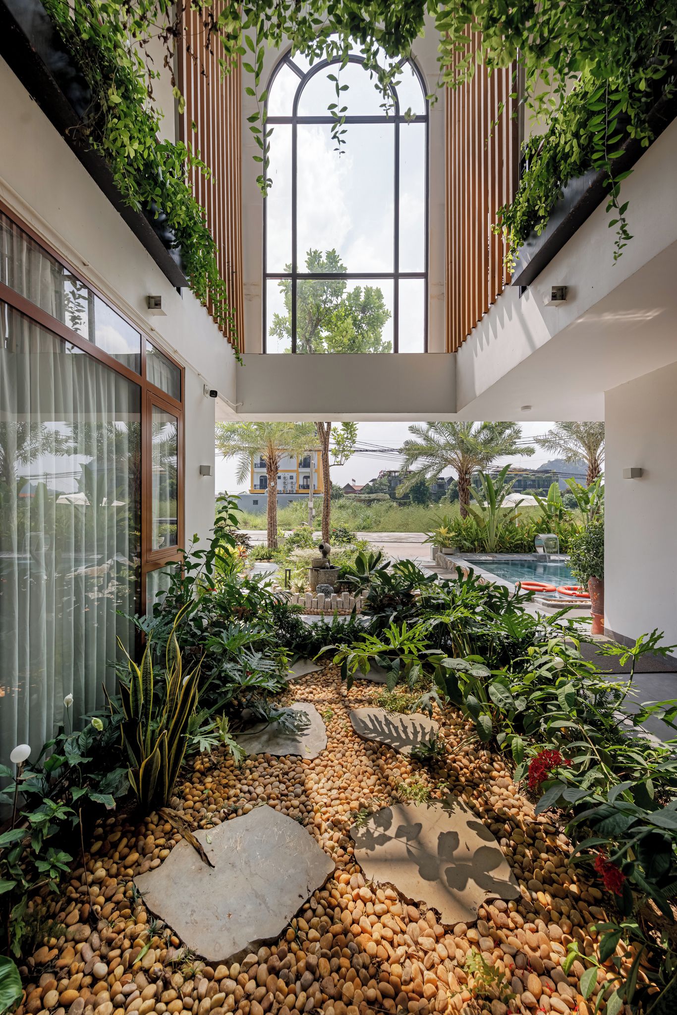 Un jardín interior espacioso con un amplio ventanal, diversas plantas y un sendero de guijarros.