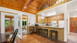 A spacious kitchen with wooden cabinets, a central island with bar stools, and a view of the outdoors. - New in 2026! Glidden Pines -Beach Access -July/August Dates Still Avail! (Sturgeon Bay)