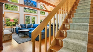 A spacious living area with a wooden staircase, large windows, and a blue sofa. - New in 2026! Glidden Pines -Beach Access -July/August Dates Still Avail! (Sturgeon Bay)