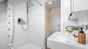Ein modernes Badezimmer mit Dusche, Waschbecken und Holz-Seifenspender sowie Handtuchhalter.