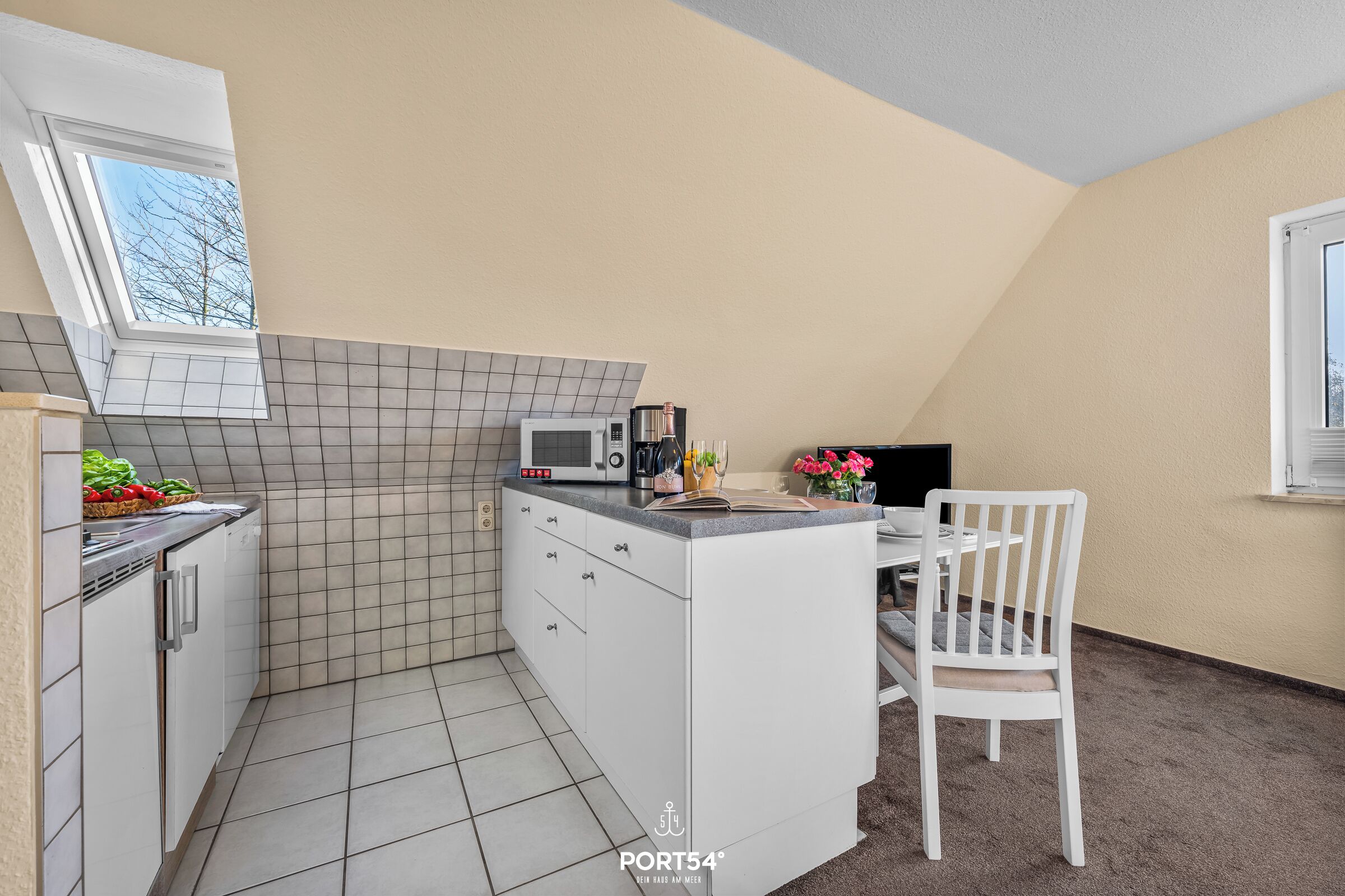 Eine kompakte Küche mit Mikrowelle, Toaster und einer kleinen Essecke mit einem Stuhl.