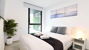 A modern bedroom with a large bed, a bedside table with a lamp, and a window with blinds.