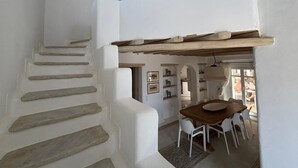 A staircase with white walls and wooden steps leading to a dining area with a wooden table and white chairs. - Topos exclusive Mykonos-villa Kymothoe (Agios Ioannis Diakoftis)