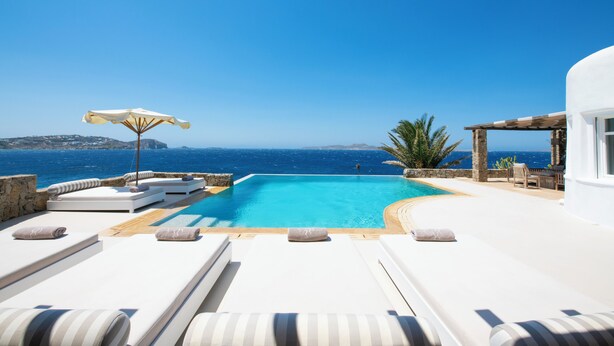 A poolside area with lounge chairs and a view of the sea. - Topos exclusive Mykonos-villa Kymothoe (Agios Ioannis Diakoftis)