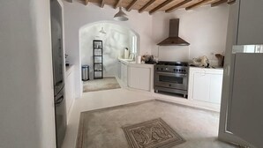 A kitchen with white cabinets, a stainless steel oven, and a wooden ceiling. - Topos exclusive Mykonos-villa Kymothoe (Agios Ioannis Diakoftis)