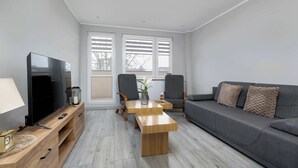 Un soggiorno moderno con televisore a schermo piatto, tavolino in legno, divano grigio e due poltrone.