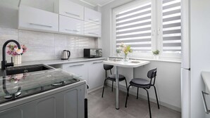 Una cucina moderna con mobili bianchi, un piano di lavoro in vetro e due sedie nere attorno a un tavolino.