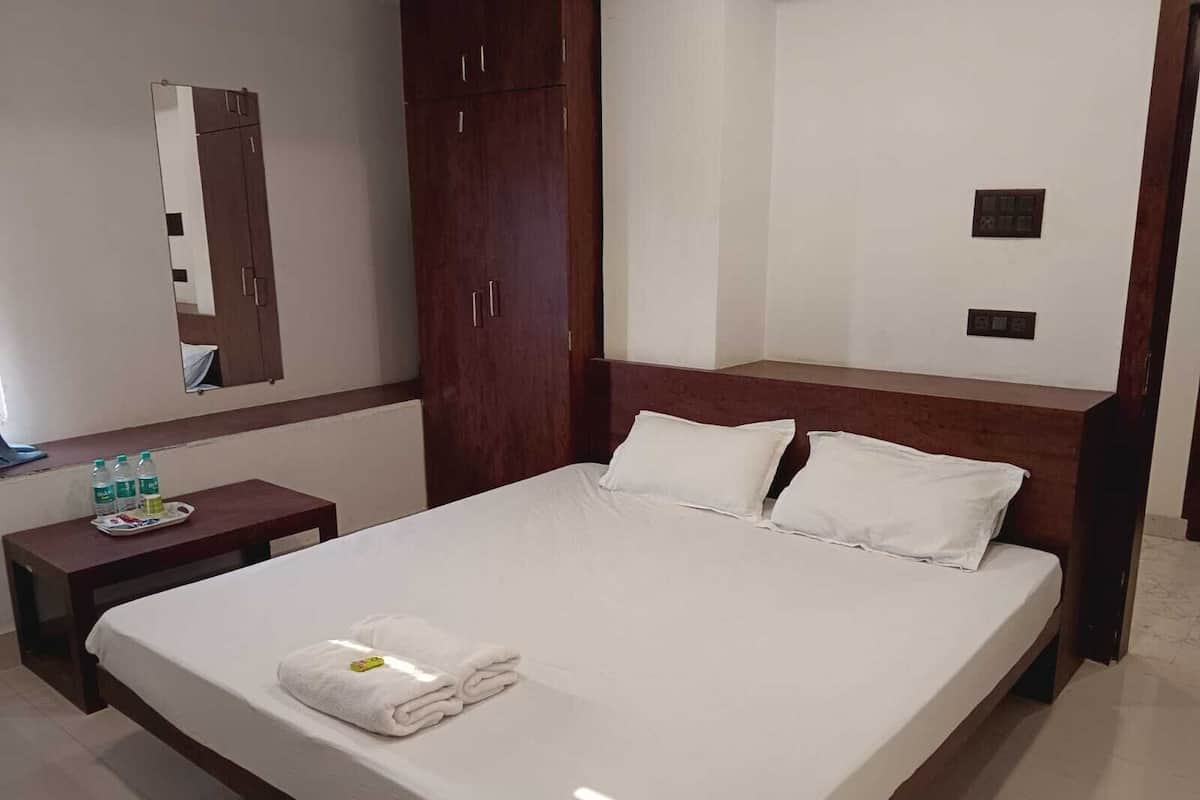 Une chambre d’hôtel comprenant un lit, une armoire en bois, une table de chevet avec un plateau d’articles de toilette et un miroir fixé au mur.