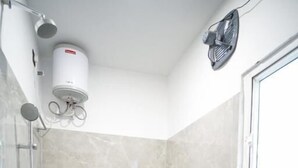 A small bathroom with a toilet, a sink, a shower, and a wall-mounted fan. - Royal Majestic Lodge  (Guwahati)