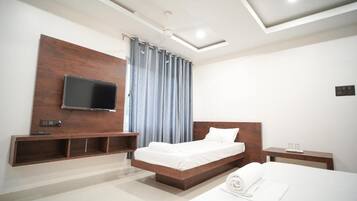 Una camera d'albergo moderna con una testiera in legno, una TV a schermo piatto montata a parete, un comodino con una lampada e un letto rifatto con un asciugamano arrotolato.