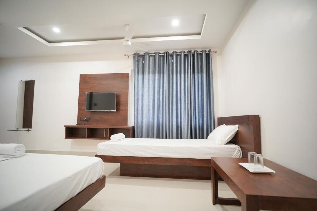 A modern hotel room with a large bed, a bedside table, a TV mounted on the wall, and a ceiling fan.