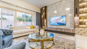 A modern living room with a glass coffee table, a large flat-screen TV, and a sofa. - 4BR + Maid’s Room Villa Near Nad Al Sheba Mall, With Easy Access to Major Dubai Attractions (Dubai)