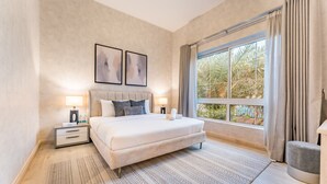 A bedroom with a large bed, bedside tables with lamps, a window with curtains, and a view of palm trees. - 4BR + Maid’s Room Villa Near Nad Al Sheba Mall, With Easy Access to Major Dubai Attractions (Dubai)