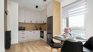 A modern kitchen with white cabinets, a black refrigerator, and a dining area with a table set for two.