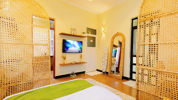 A room with a bed, television, shelves, and a mirror. - Tadre House's (Arusha)