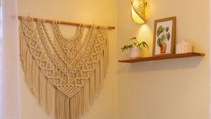 A macrame wall hanging, a wooden shelf with potted plants, and a framed picture. - Tadre House's (Arusha)