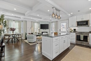 A spacious kitchen with white cabinetry, a large island, and a built-in oven. - Somerville Gem! Steps to Union Sq + Transit (Somerville)