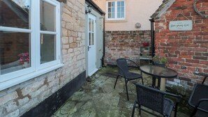 A stone building with a white door, a small window, and a brick wall with a sign that says "love grows here". - The Corner Cottage (Wotton-under-Edge)