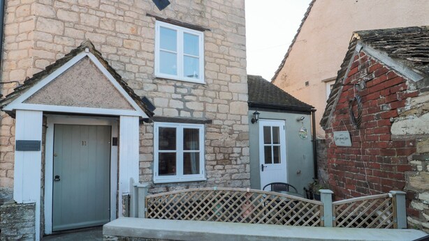 A stone building with a grey door, a small window, and a white door. - The Corner Cottage (Wotton-under-Edge)