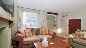 A cozy living room with a sofa, a wooden coffee table, and a window with curtains. - The Corner Cottage (Wotton-under-Edge)