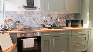 A kitchen with green cabinets, a black stove, a microwave, and a patterned backsplash. - The Corner Cottage (Wotton-under-Edge)