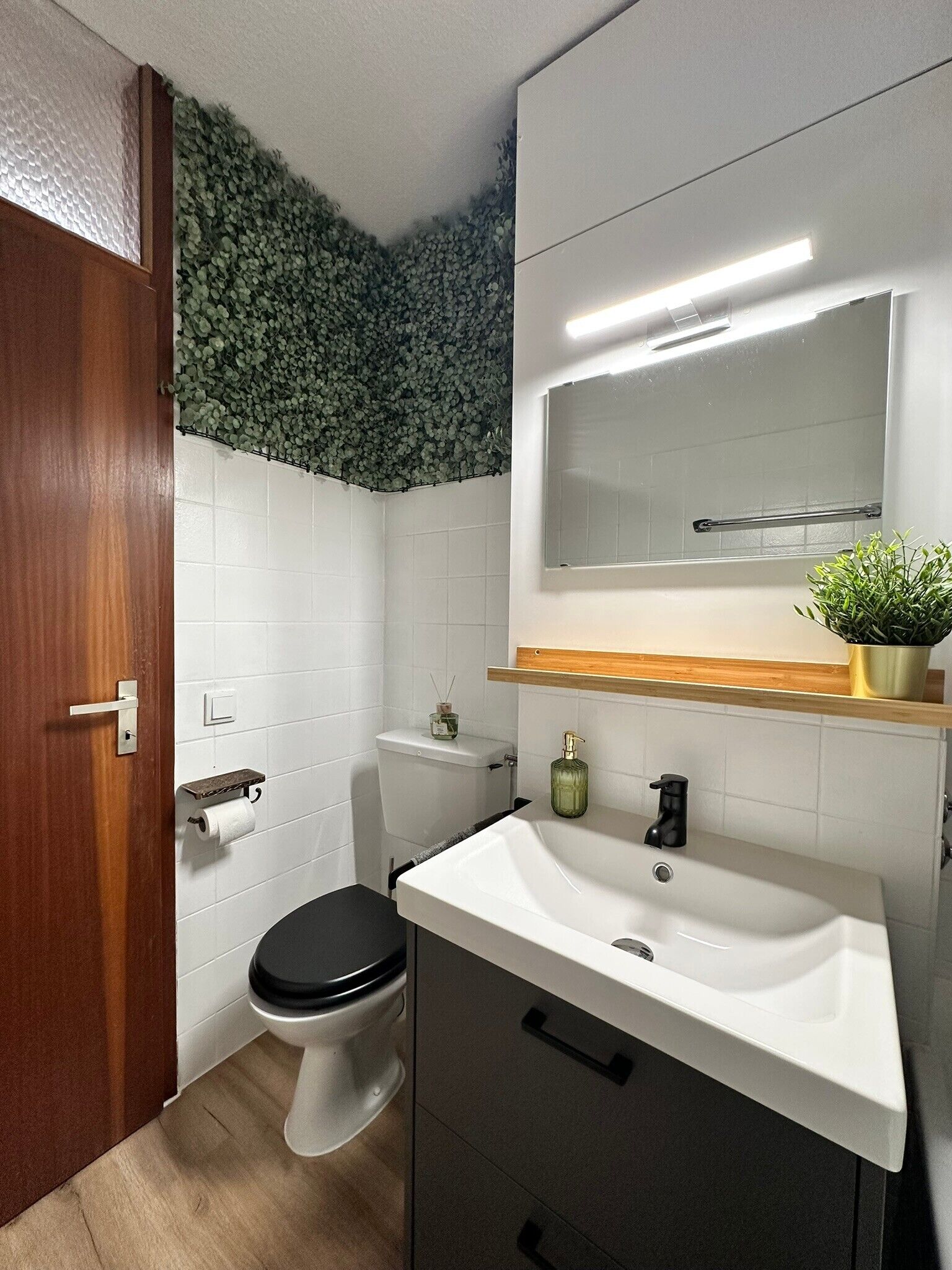 A bathroom with a toilet, sink, mirror, and a wooden door.