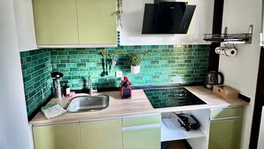 A compact kitchen with a green backsplash, a black range hood, and a hanging light fixture.
