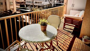 Un balcon avec une table ronde en verre, des chaises en osier, un canapé blanc et une plante en pot.