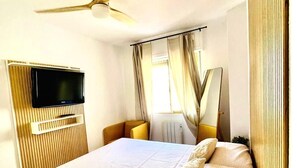 Une chambre à coucher avec un lit, une télévision, un ventilateur de plafond et des rideaux.