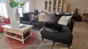 Olohuoneessa on punainen nojatuoli, harmaa sohva, sohvapöytä ja suuri huonekasvi.