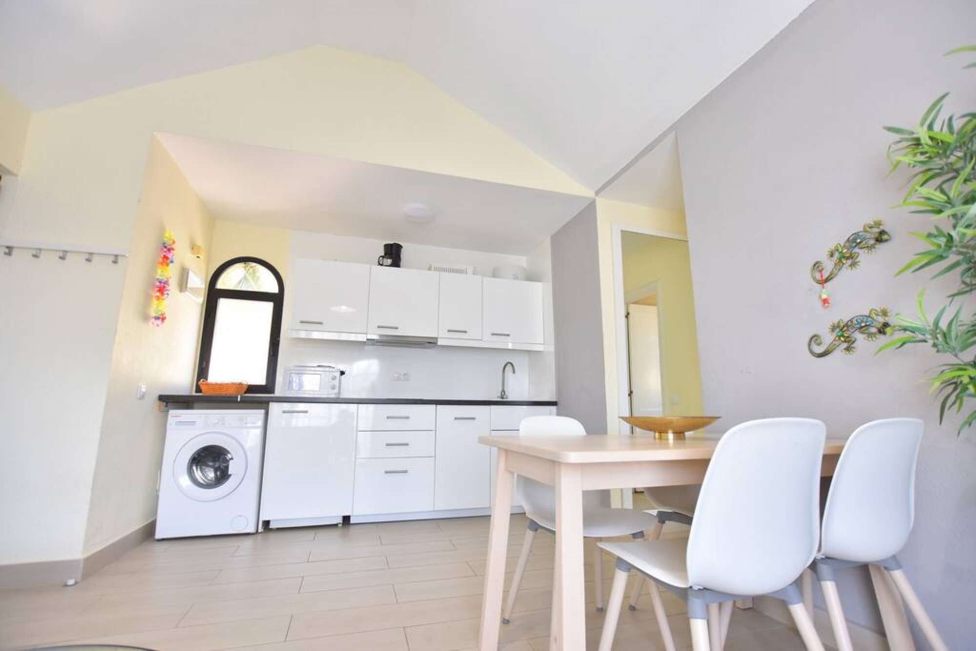A compact kitchen with white cabinets, a washing machine, and a dining area with a table and chairs.