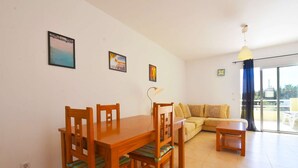 Uma sala de jantar com mesa e cadeiras de madeira, um sofá e um abajur. Há três quadros na parede.