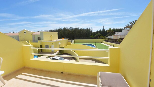 Varanda amarela com vista para uma piscina e edifícios próximos.