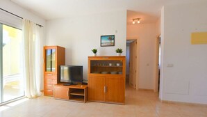 Uma sala de estar com televisão, armários de madeira e uma pequena planta na parede.