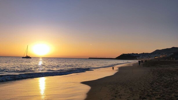 A beach at sunset with a sailboat on the water and people walking along the shore. - Book Jet - NinoMar Heart Morro Jable (Morro Jable)