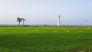 A grassy field with a lighthouse in the background and a sculpture in the foreground. - Book Jet - NinoMar Heart Morro Jable (Morro Jable)