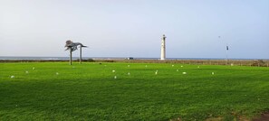 Ein grünes Feld mit einem Leuchtturm im Hintergrund und einer Skulptur im Vordergrund.